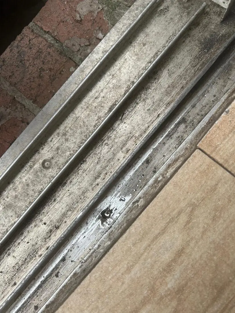 Close-up of a worn and damaged sliding door track being assessed for repair or custom fabrication